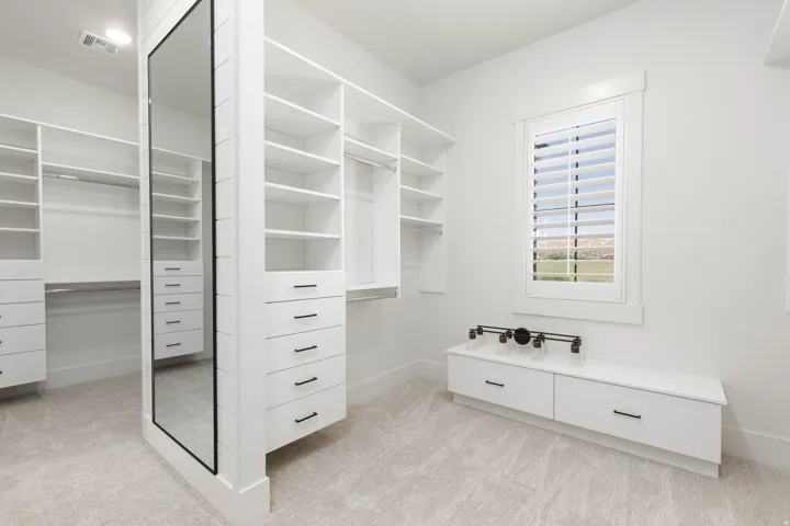 Built-in storage solutions, full-length mirror, window with plantation shutters, custom cabinetry, and neutral-toned carpeting
