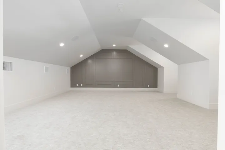 Sloped ceiling design with recessed lighting, integrated wall paneling, and light-toned carpeting