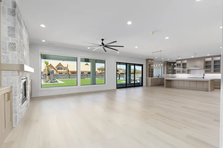 Spacious open-concept interior with light wood-finish flooring, recessed lighting, and a prominent stone-clad fireplace