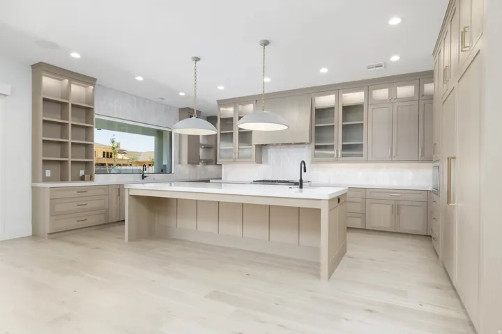 Kitchen featuring extensive light wood-tone cabinetry, a central island with a white countertop and sink, light wood-finish flooring, a linear window above the sink, and recessed ceiling lighting