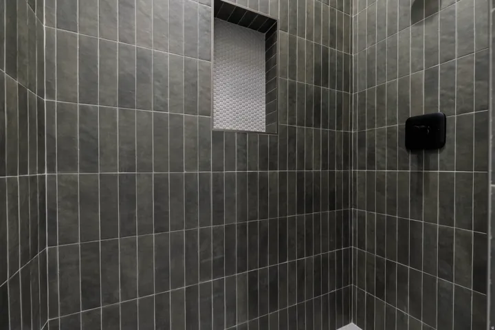 Shower enclosure featuring vertical-stacked gray rectangular tiles, a tiled niche with contrasting mosaic tile, and a matte black shower control fixture