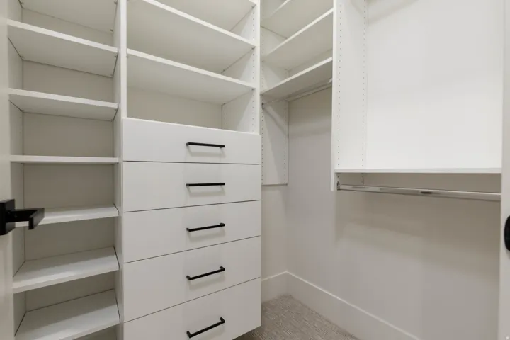 Built-in closet system featuring white shelving, multiple storage drawers, hanging rods, and a carpeted floor
