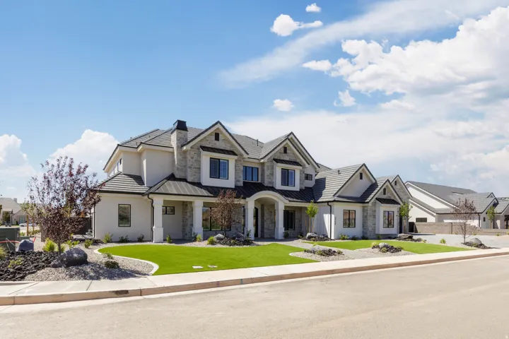 Stone and stucco exterior with multiple gables, a covered entry, dark-framed windows, a concrete tile roof, and a landscaped front yard with manicured lawn