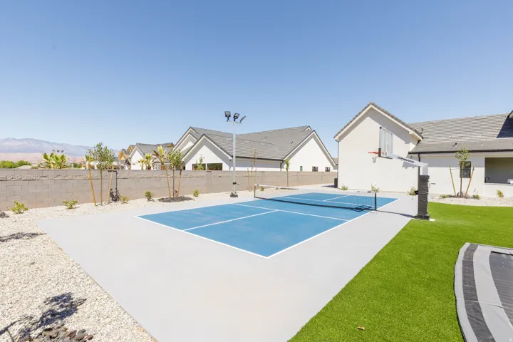 Sports court with integrated basketball hoop, artificial turf, gravel landscaping, and block perimeter fencing