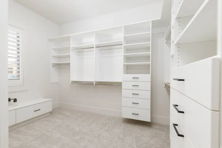 Expansive custom closet system with white cabinetry, integrated shelving, hanging rods, and multiple drawers featuring dark pull hardware