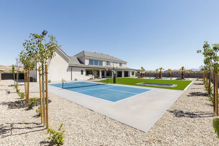 Expansive backyard featuring a multi-sport court, artificial turf lawn, inground trampoline, and a swimming pool