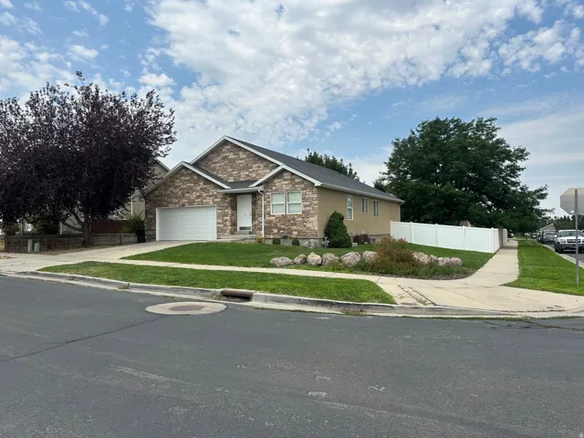 Stone and stucco exterior, attached garage, well-maintained lawn, privacy fencing, and mature trees