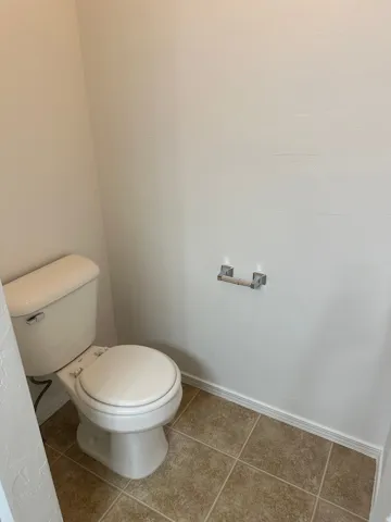 White toilet with a chrome flush lever, set on square tile flooring with a neutral finish, complemented by a wall-mounted toilet paper holder