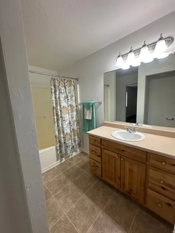 Beige tile flooring, wood-finish vanity with ample storage, single basin sink, and a combination shower/tub