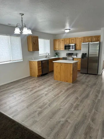 Kitchen with wood-finish cabinetry, stainless steel appliances, a center island, and a dining area with a chandelier