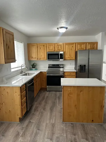 Kitchen featuring wood cabinetry, white countertops, stainless steel appliances, and wood-finish flooring