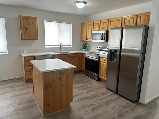 Kitchen featuring wood-finish cabinetry, white countertops, a central island, stainless steel appliances, and wood-finish flooring