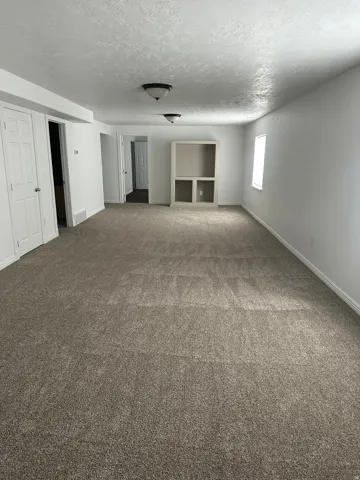Expansive room featuring neutral carpet, white walls, built-in cabinetry, and overhead lighting