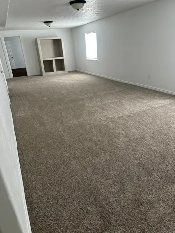 Expansive carpeted area featuring a neutral color palette, built-in shelving, white walls, and a recessed window
