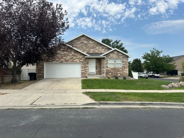 Stone facade exterior with a two-car garage, concrete driveway, and a front lawn with established landscaping.