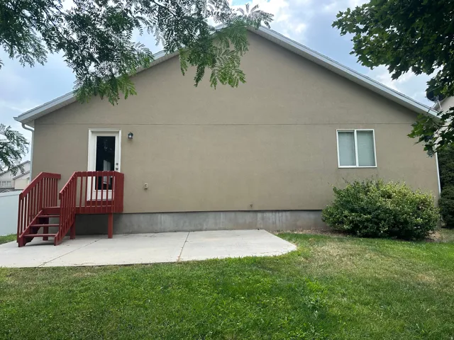 Exterior featuring a stucco finish, gable roofline, red-stained wood deck with stairs, and a concrete patio