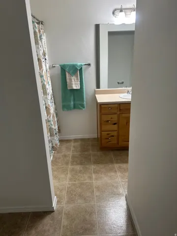 Bathroom featuring tiled flooring, a wooden vanity with a laminate countertop, and a wall-mounted mirror with integrated lighting