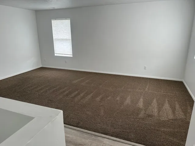 Spacious room featuring brown carpet flooring, white painted walls, and a window with blinds
