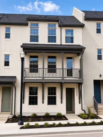 Three-story stucco exterior with a covered balcony featuring dark railings, multiple double-hung windows, and a dark asphalt shingle roof