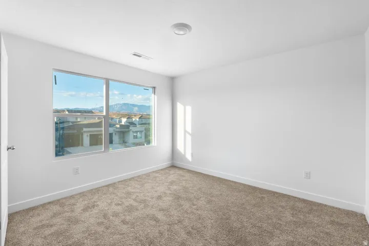 Bright room with a large window, neutral carpeting, white walls, and a ceiling-mounted light fixture