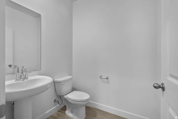 Pedestal sink with chrome faucet, wall-mounted mirror, white toilet, and wood-finish flooring