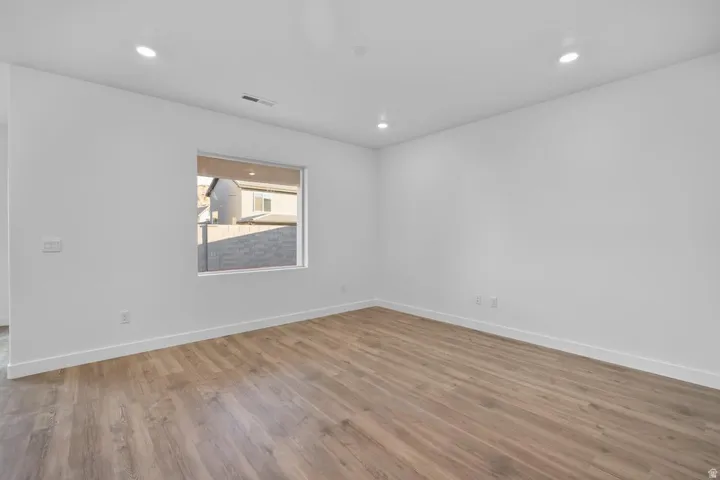 Recessed lighting illuminates the room with wood-finish flooring and a large window