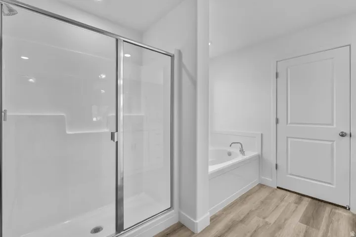 Walk-in shower with sliding glass door, built-in bathtub, white panel doors, recessed lighting, and wood-finish flooring