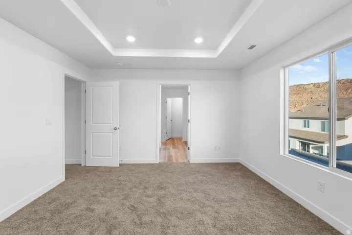 Spacious interior room featuring neutral white walls, recessed ceiling lighting, neutral-tone carpet flooring, and multiple white panel doors providing access to adjoining spaces