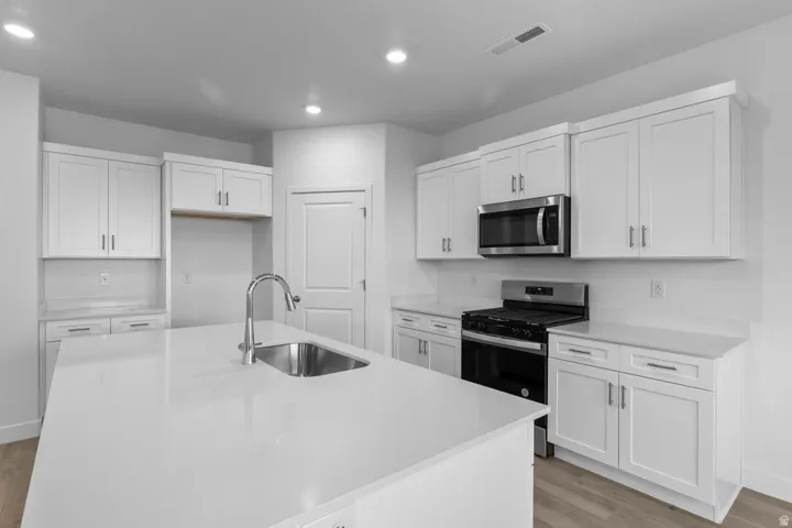 Kitchen featuring an island with an undermount sink, stainless steel appliances, white cabinetry, and recessed lighting