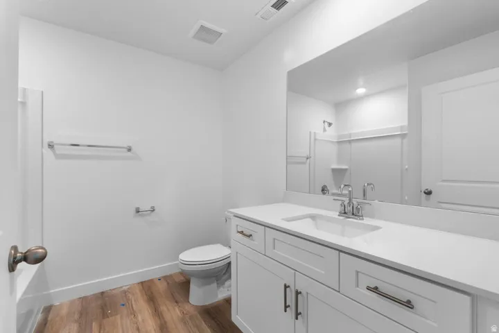 White shaker-style cabinetry with dark bronze hardware, white integrated sink with chrome faucet, wide vanity mirror, and wood-finish flooring