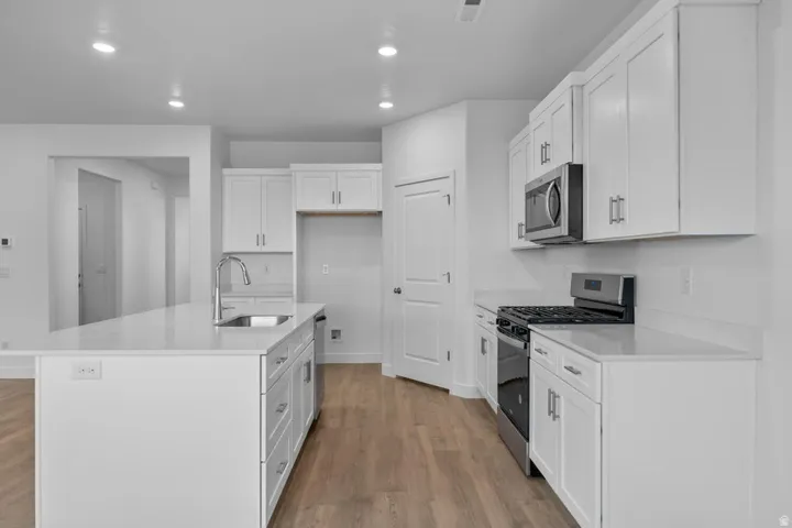 Kitchen featuring a gas range, stainless steel microwave, white cabinetry, a large center island with a sink, and wood-finish flooring