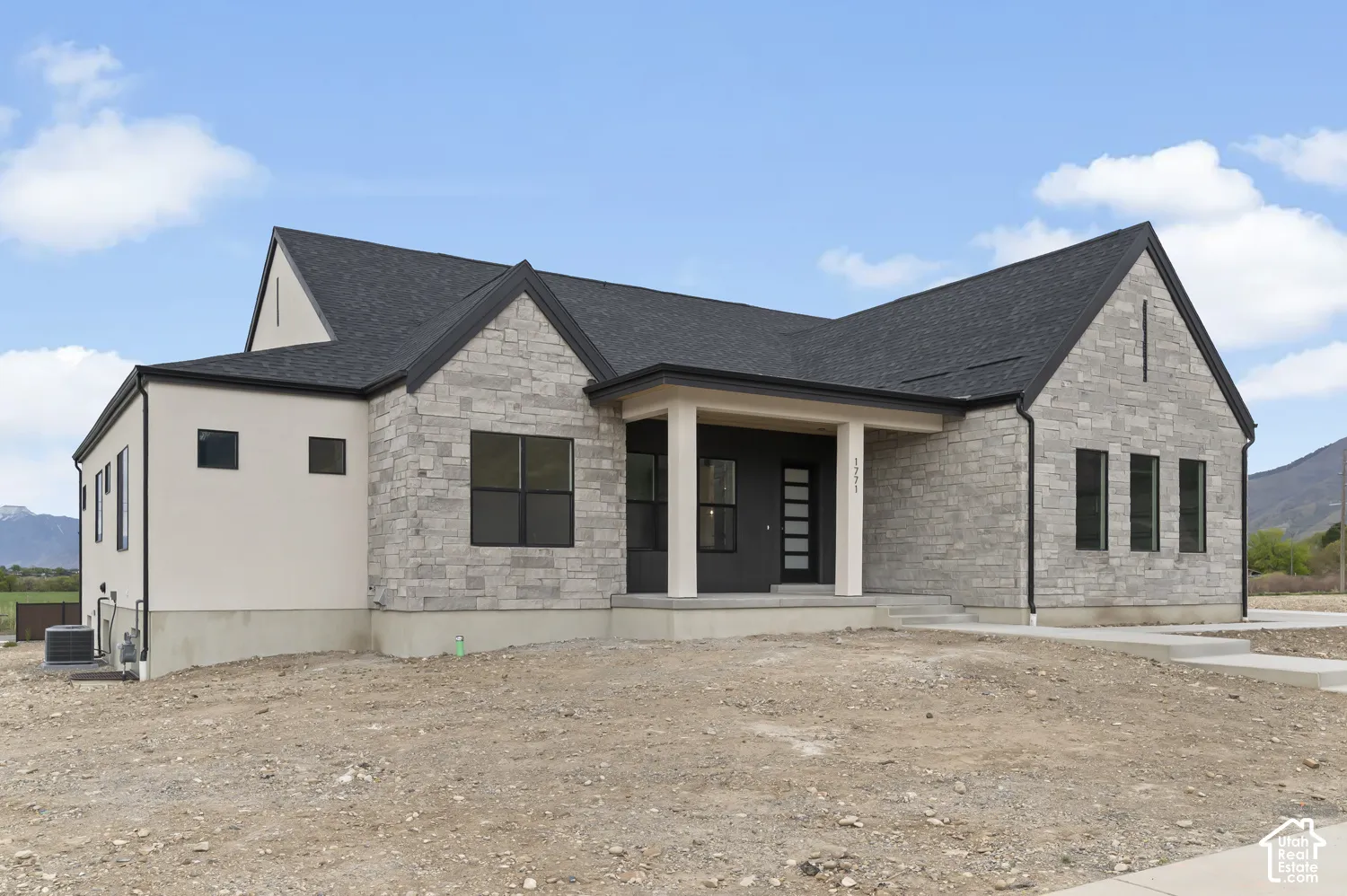Modern architectural design featuring varied exterior finishes, a dark shingle roof, black-framed windows, and an inviting covered entry