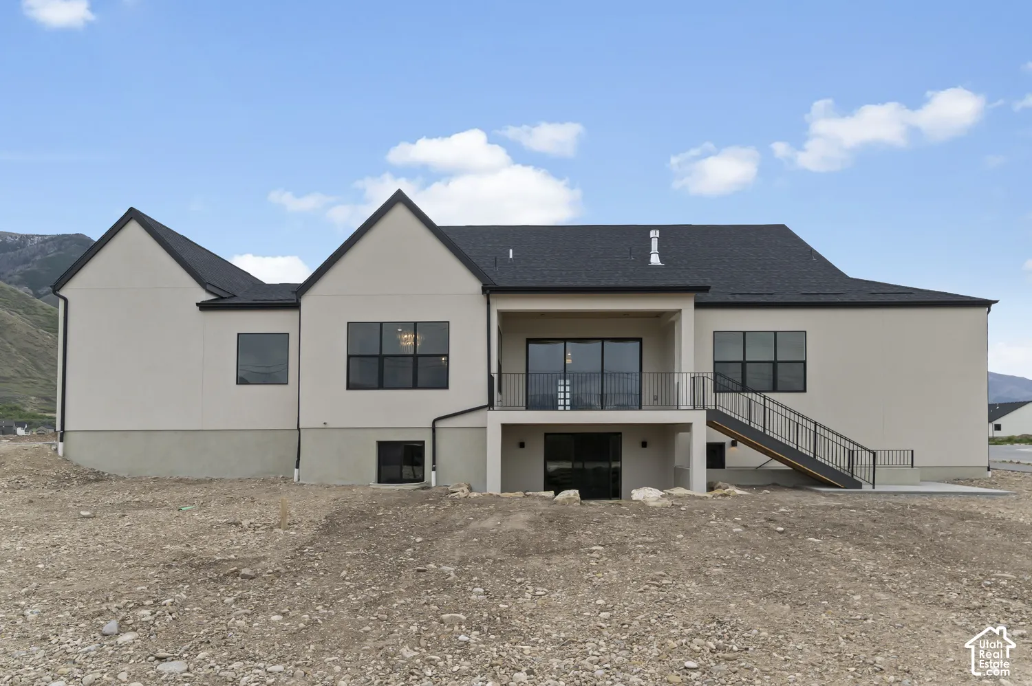Contemporary stucco exterior with a dark shingle roof, black-framed windows, and a covered balcony with a metal railing