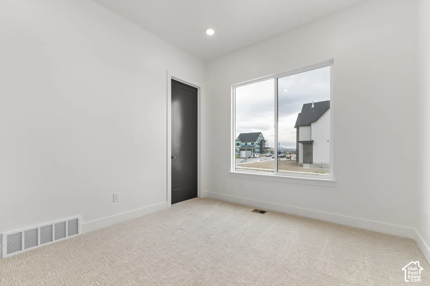 Recessed lighting, neutral carpeting, white walls, dark interior door, large window with white trim
