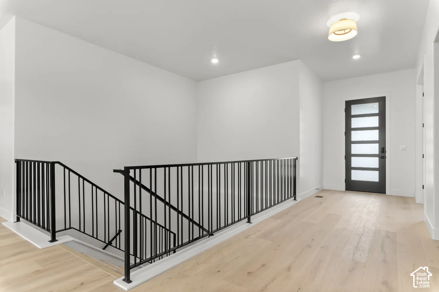 Light wood-finish flooring, white walls, and a modern black entry door with frosted glass panels