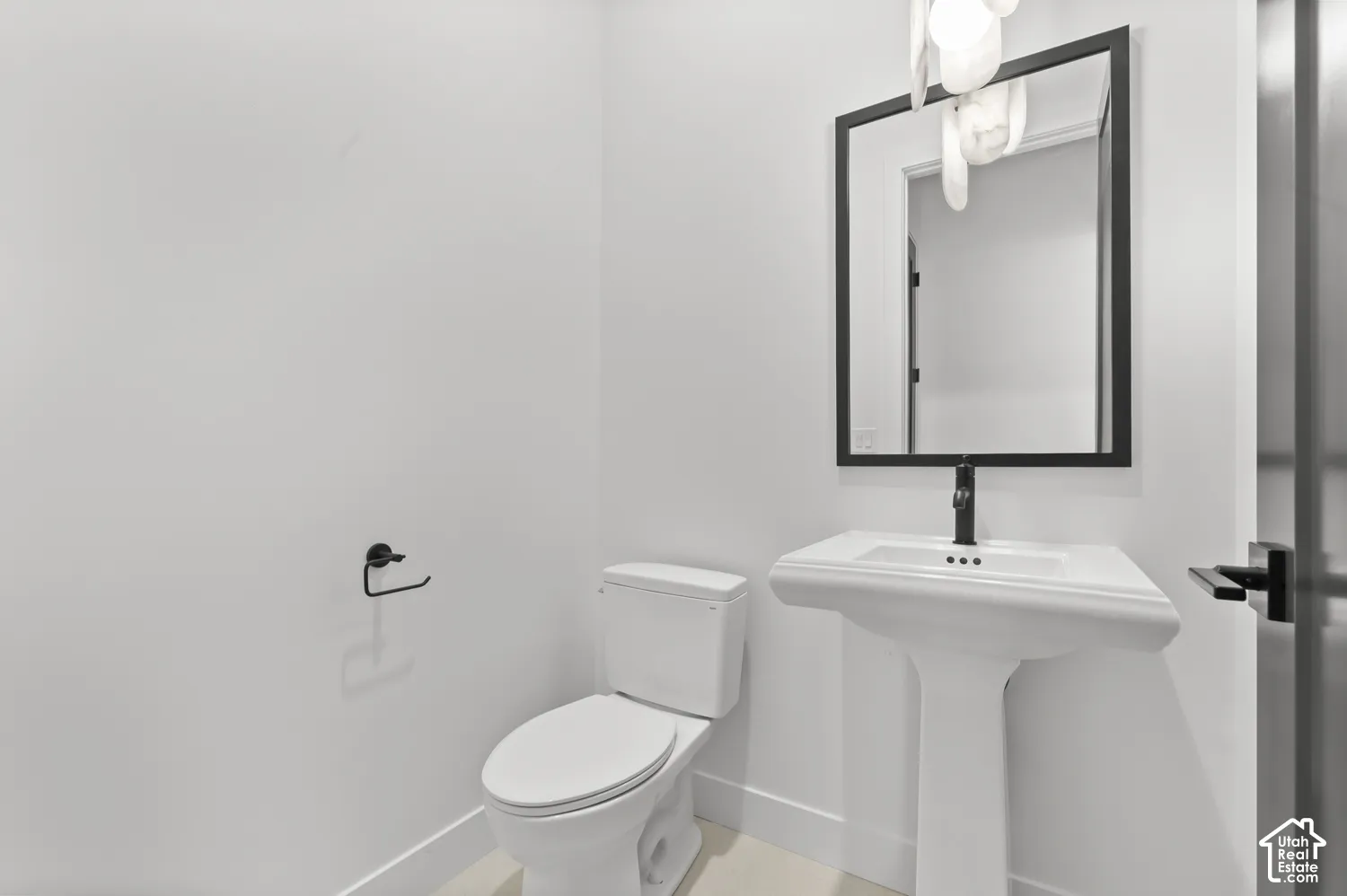 Pedestal sink with a sleek black faucet, a framed mirror, and a white toilet