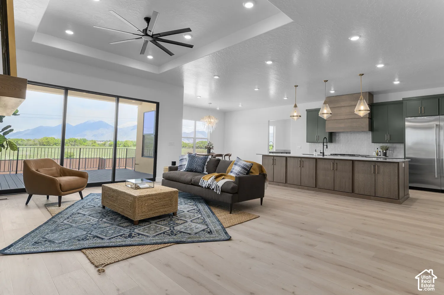 Open-concept living space featuring wood-finish flooring, a tray ceiling with a modern ceiling fan, and recessed lighting