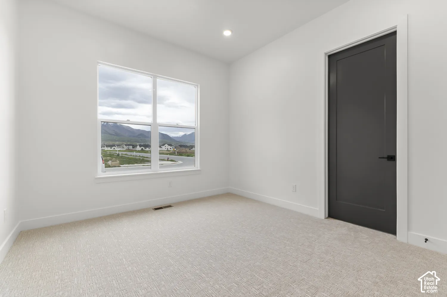 Recessed lighting, large window with mountain scenery, neutral-toned carpet, white painted walls, and dark interior door with matte black hardware