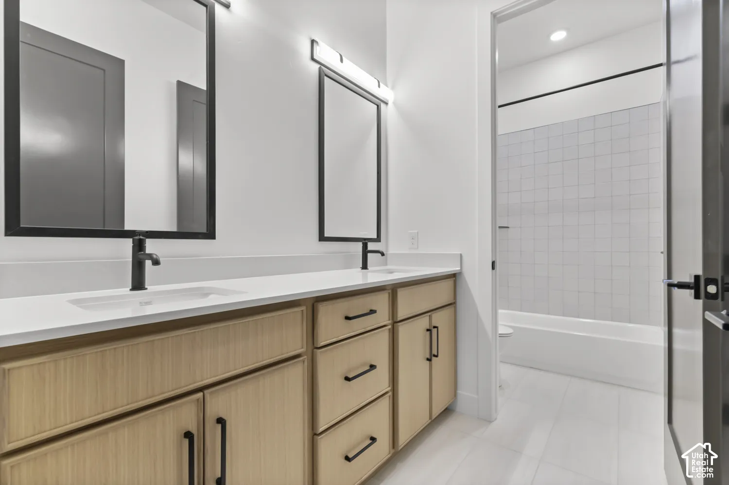 Dual vanity with light wood-finish cabinetry, matte black fixtures, rectangular sinks, and white countertops