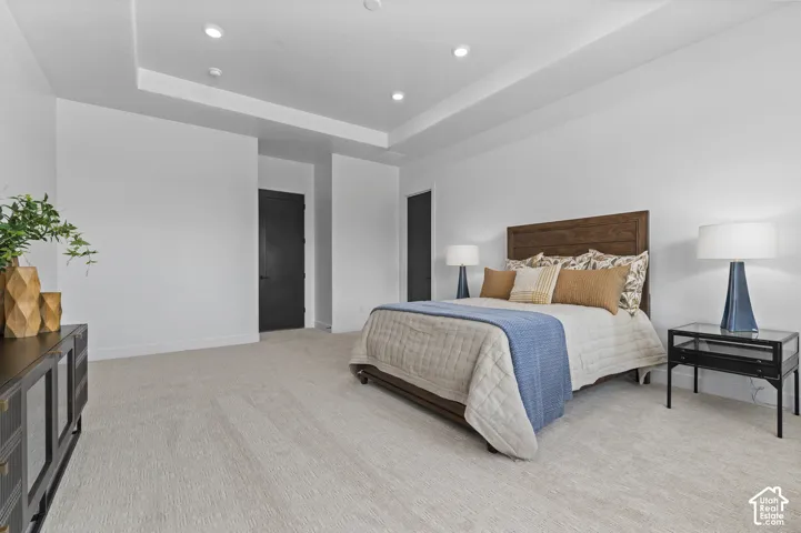 Tray ceiling with recessed lighting, light-toned carpeting, dark wood-finish headboard, and dark interior doors