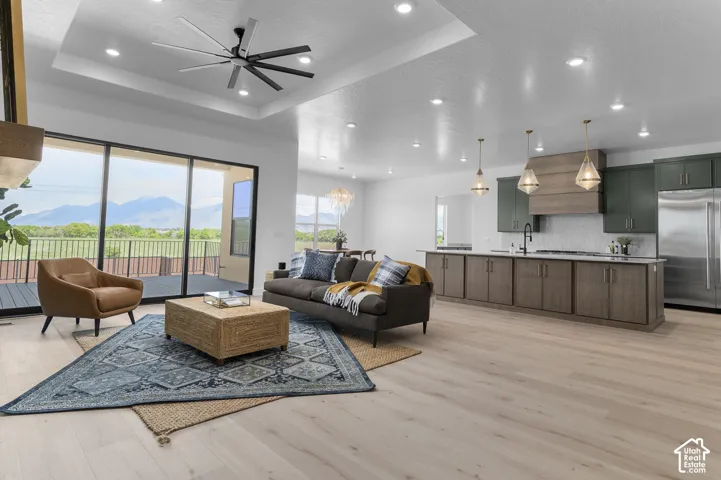 Open-concept living space featuring wood-finish flooring, a tray ceiling with a modern ceiling fan, and recessed lighting