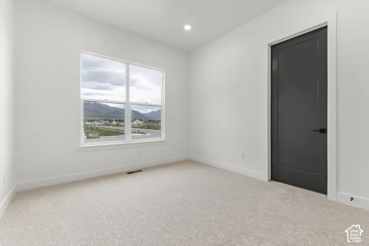 Recessed lighting, large window with mountain scenery, neutral-toned carpet, white painted walls, and dark interior door with matte black hardware