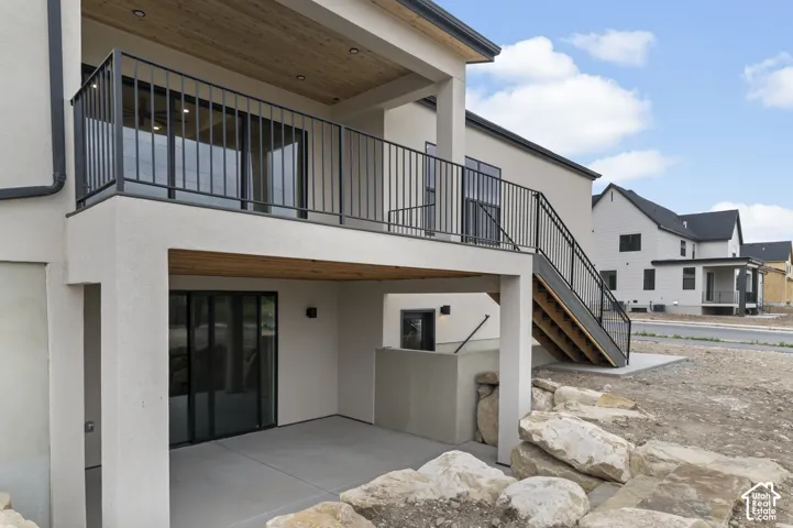 Upper-level balcony with black metal railing, covered patio below, wood-finish ceiling on upper balcony, and exterior stairs with black metal railing