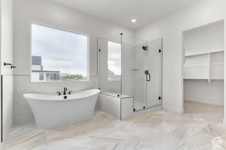 Freestanding soaking tub with matte black fixtures, glass-enclosed shower with subway tile, large window, and built-in closet shelving