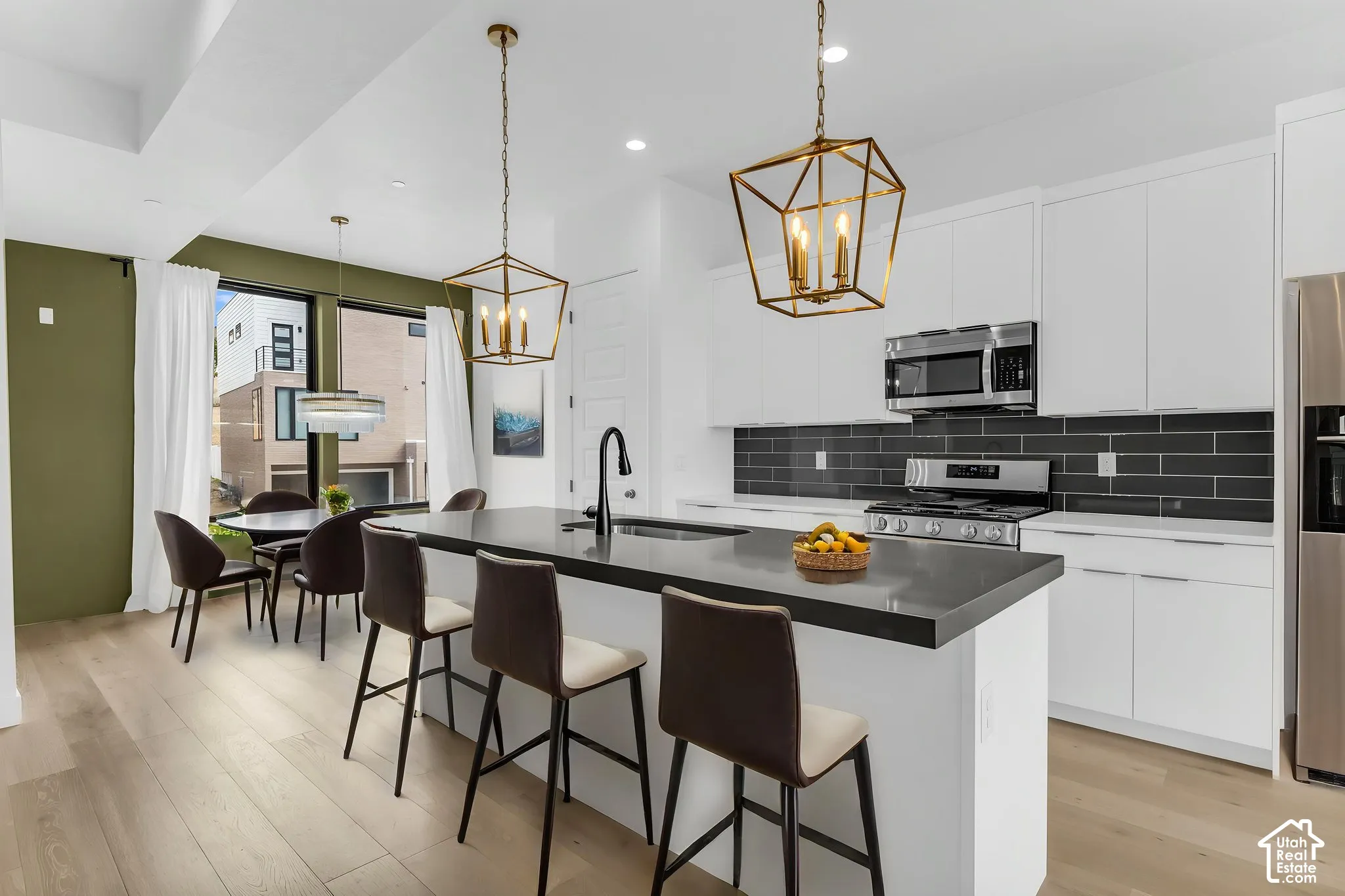 Modern kitchen featuring an expansive center island with a dark countertop, white cabinetry, integrated stainless steel appliances, and wood-finish flooring