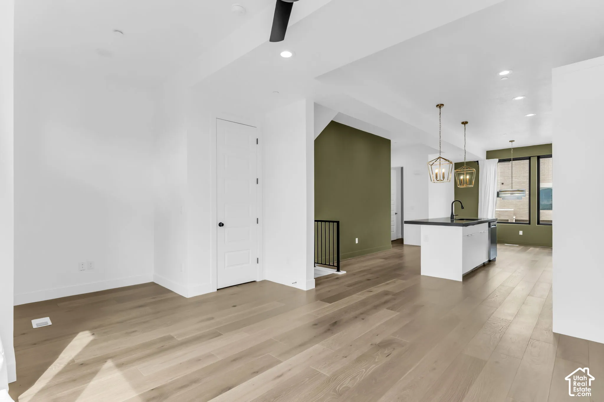 Wood-finish flooring throughout, recessed lighting, and a kitchen island with a black countertop and pendant lighting
