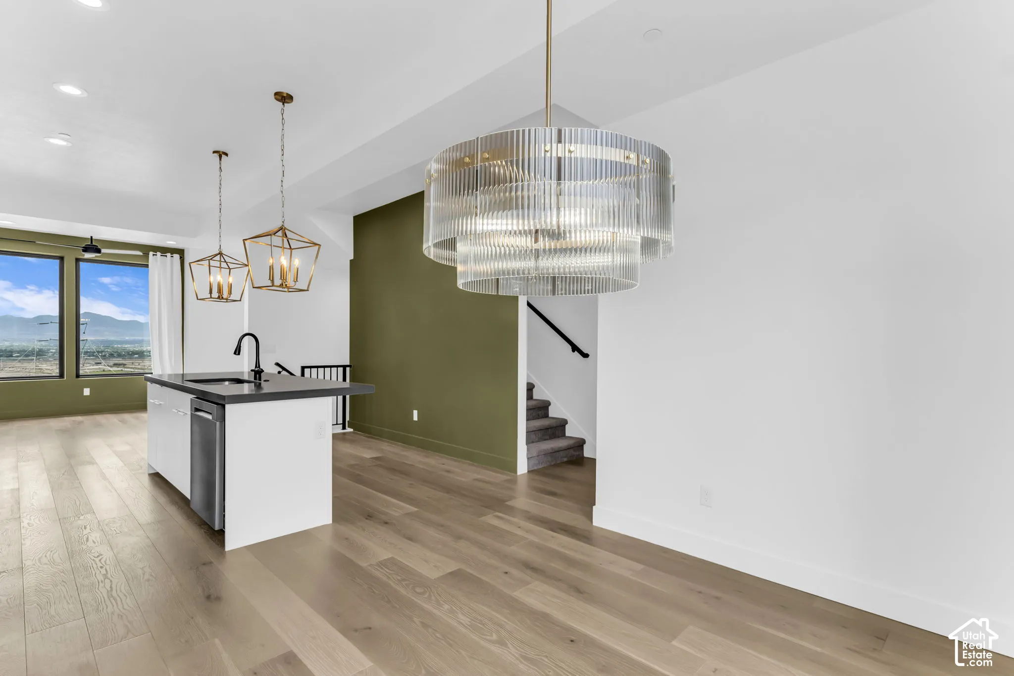 Open-concept living space with wood-finish flooring, a kitchen island featuring a sink and dishwasher, and large windows