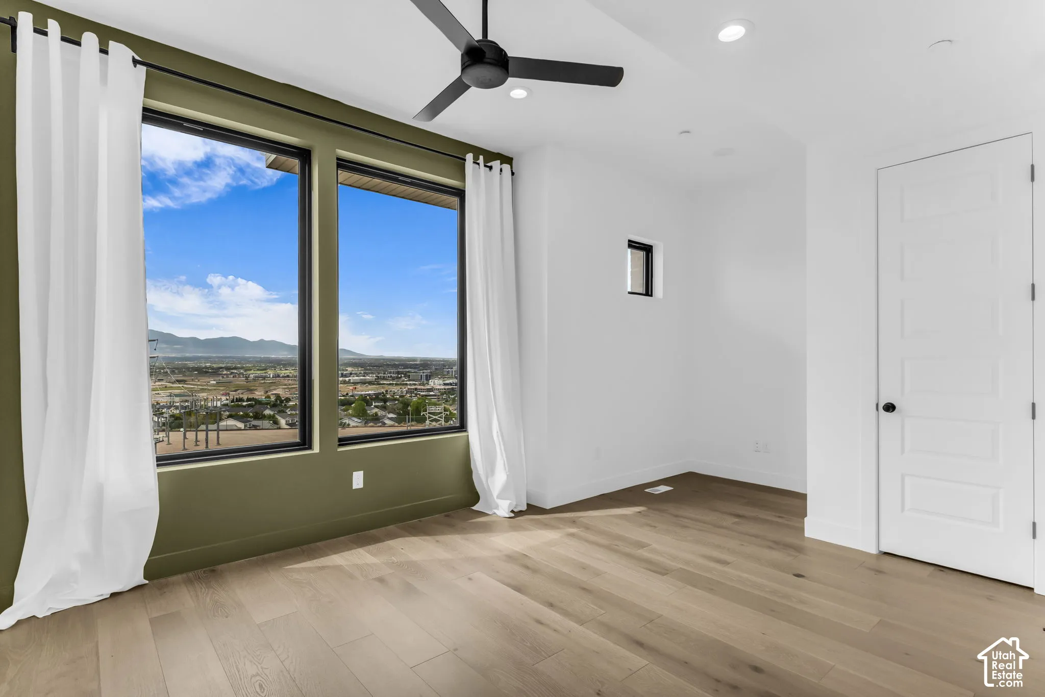 Expansive windows showcasing mountain scenery, wood-finish flooring, ceiling fan, recessed lighting, and a paneled door