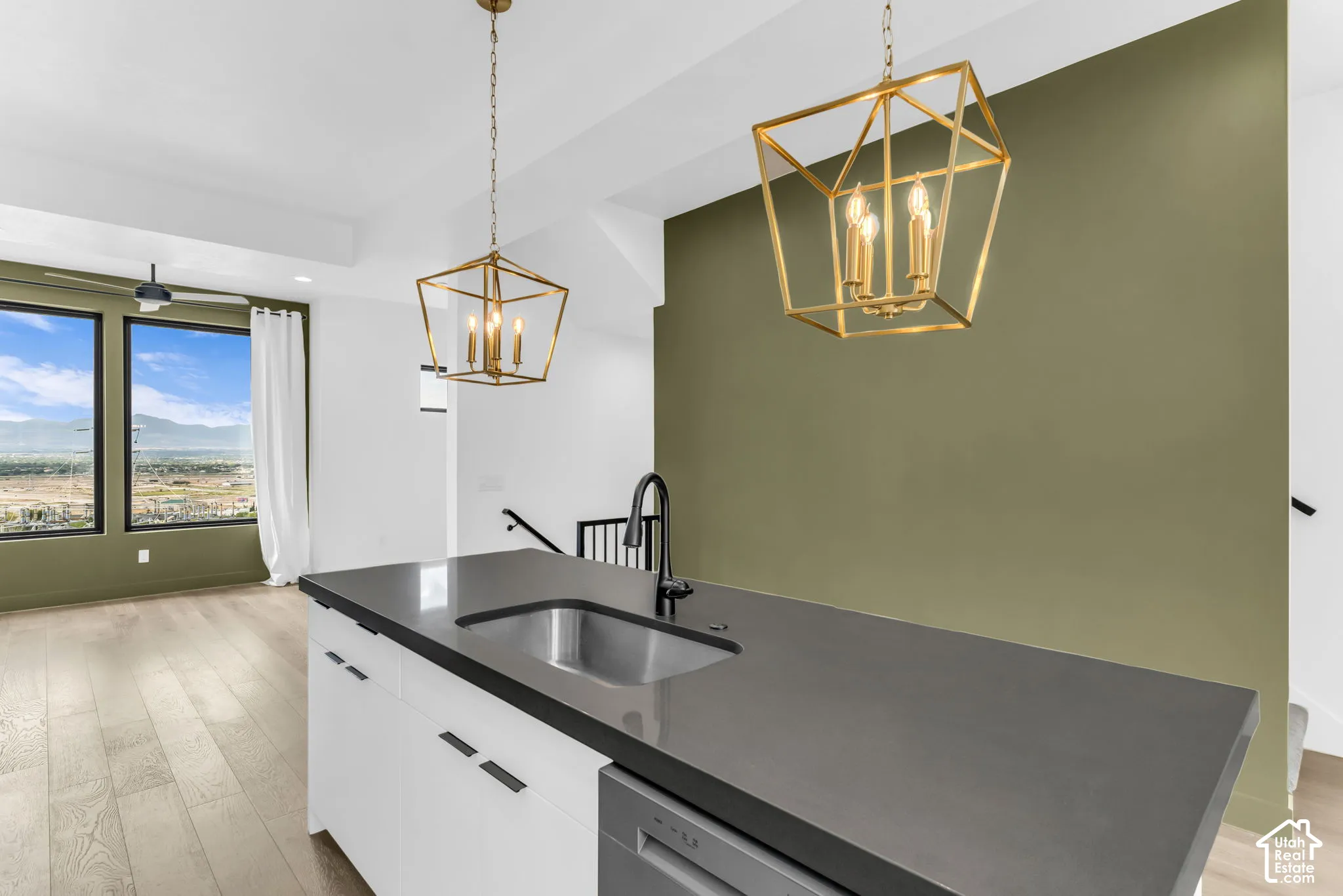 Kitchen island with integrated sink, modern gold-toned lighting fixtures, wood-finish flooring, and large windows
