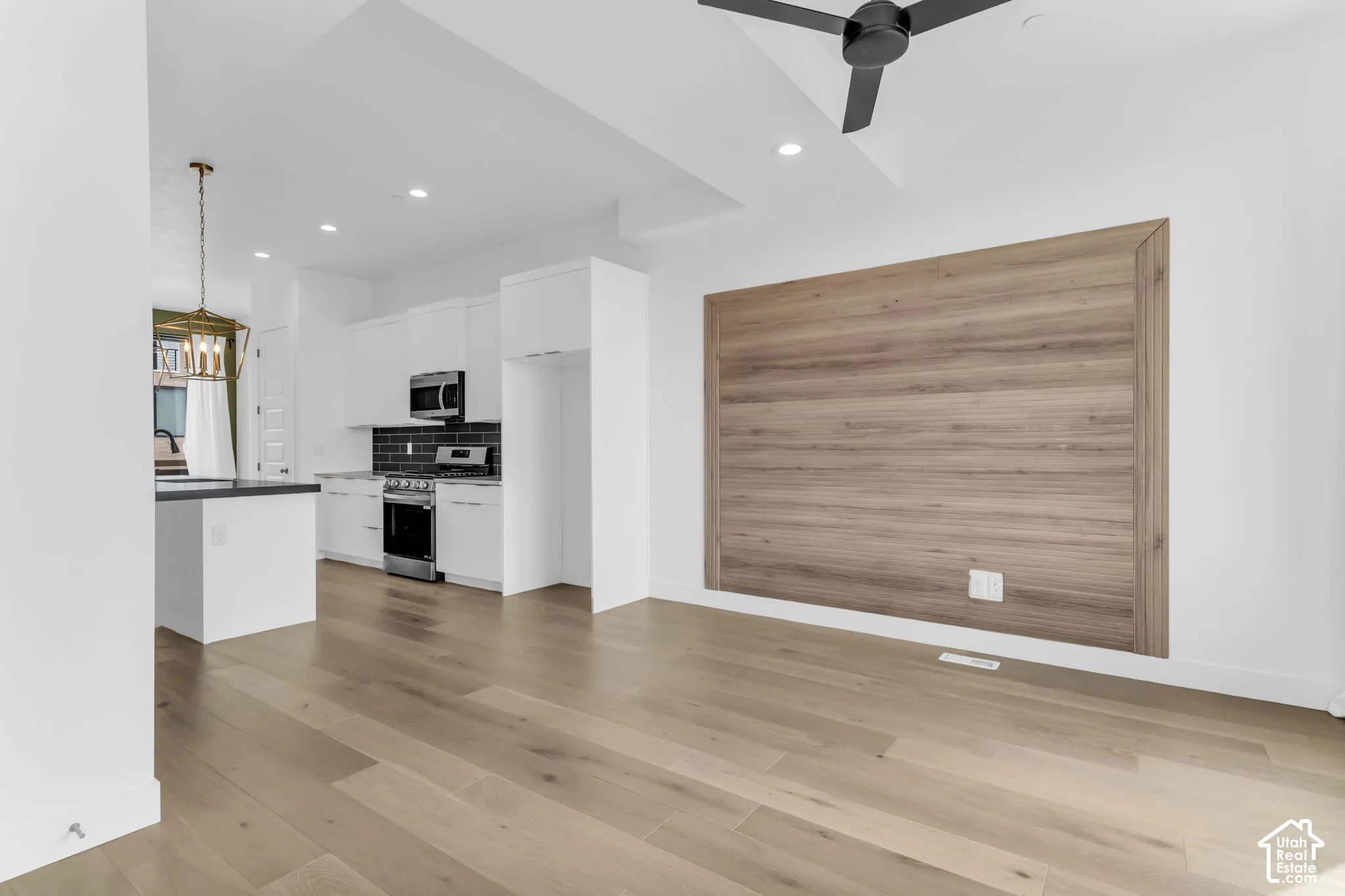 Open-concept living area with wood-finish flooring, a contemporary ceiling fan, and a wood-paneled accent wall